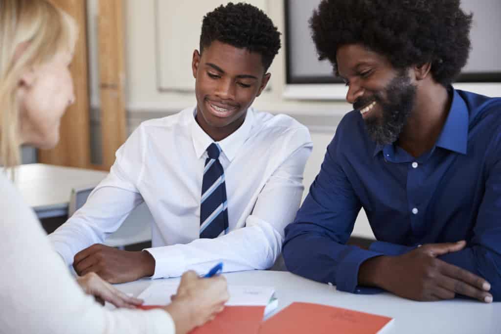 Padre e hijo adolescente discutiendo con una profesora en la reunión de padres de la escuela secundaria