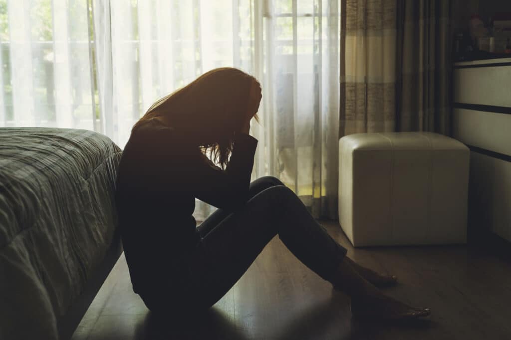 mujer deprimida sentada con la cabeza entre las manos en el dormitorio oscuro