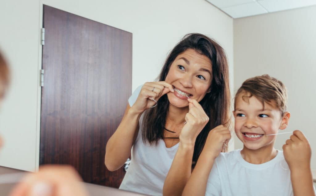 Madre e hijo limpiándose los dientes con hilo dental